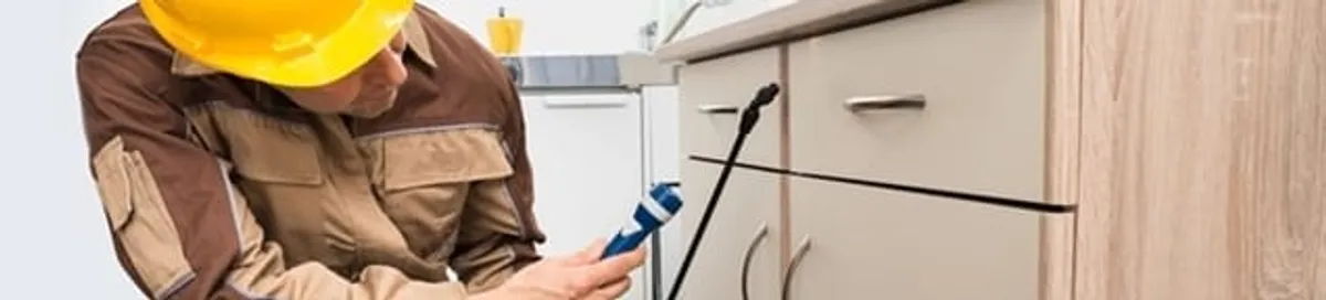 Roach exterminator applying treatment under kitchen cabinets in Scottsdale, AZ