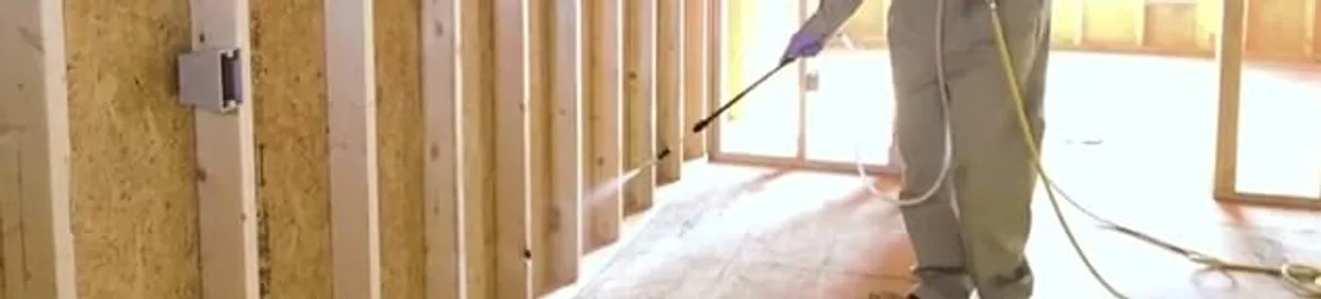 Termite treatment technician applying spray along framing and unfinished walls in Scottsdale, AZ
